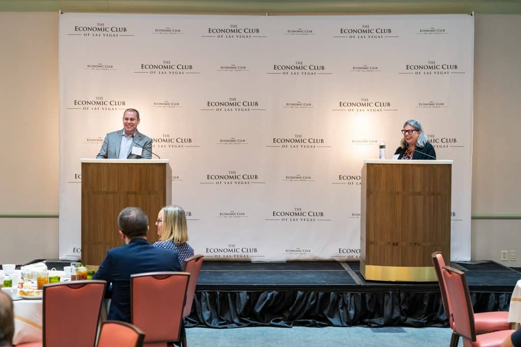 A man and woman speak at podiums on a stage with a backdrop of "The Economic Club of Las Vegas" logos.