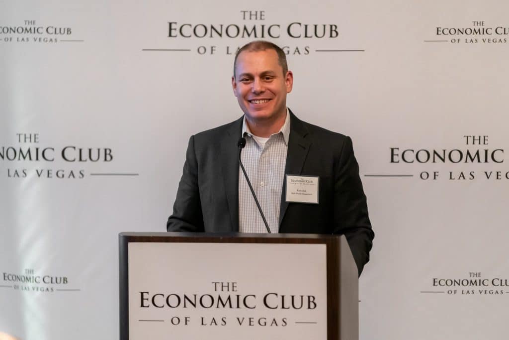 A smiling man in a suit and striped shirt stands at a podium with "The Economic Club of Las Vegas" logo.