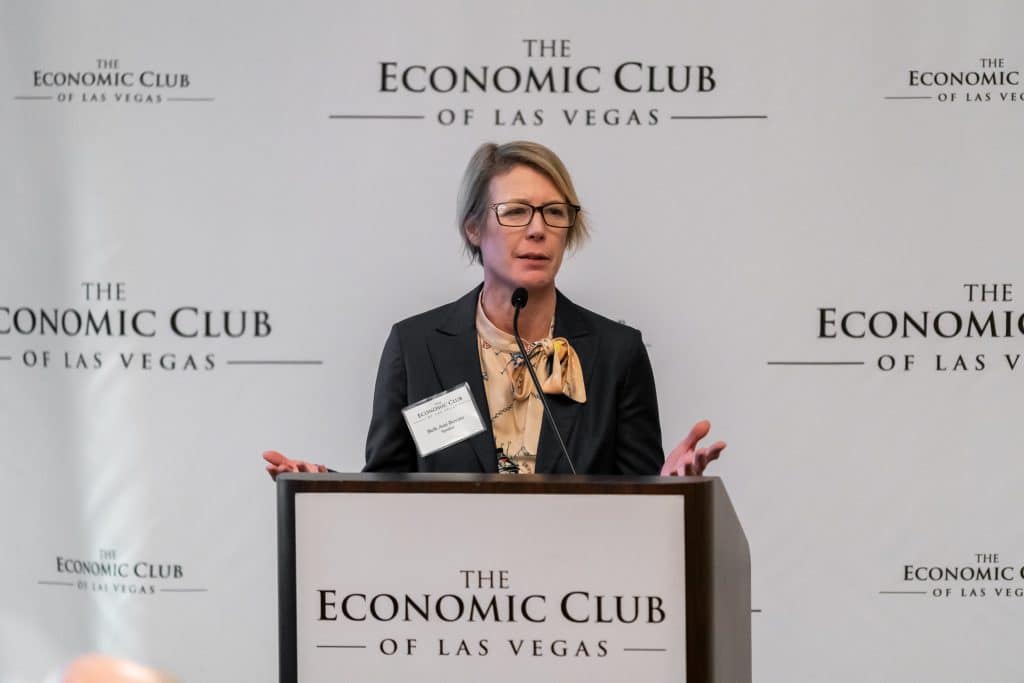 A woman with glasses and short blonde hair speaks at a podium with "THE ECONOMIC CLUB OF LAS VEGAS" on it.