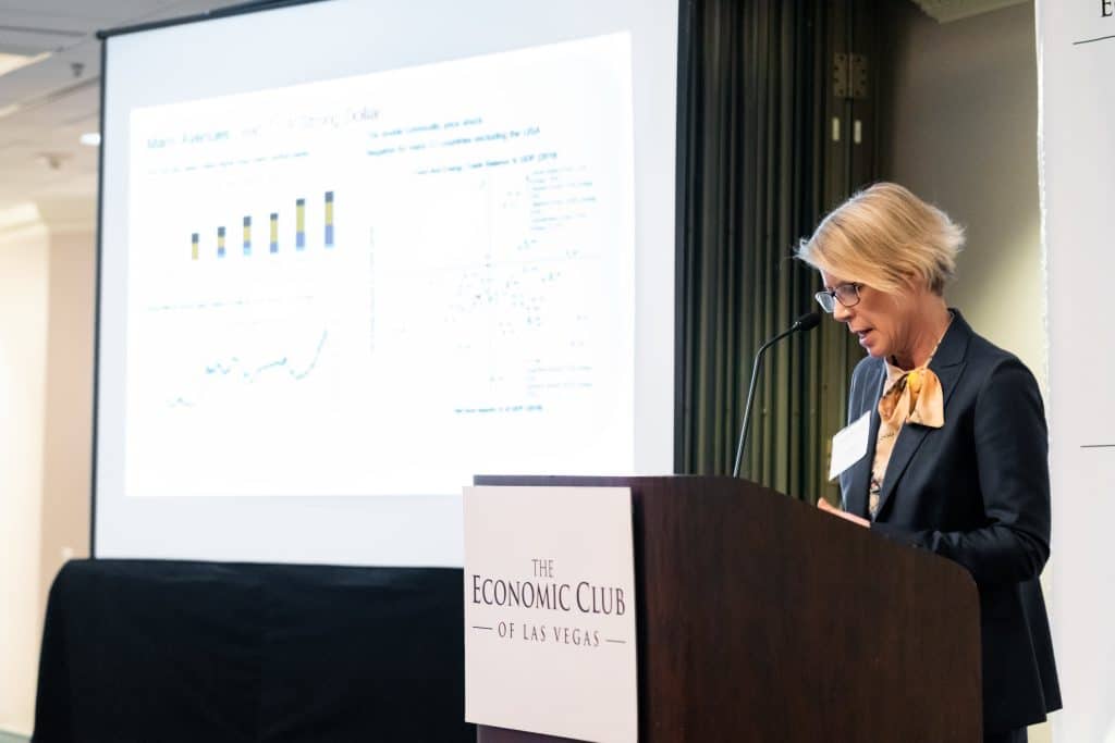 A woman in a suit and bow tie speaks at a podium with "THE ECONOMIC CLUB OF LAS VEGAS" on it.