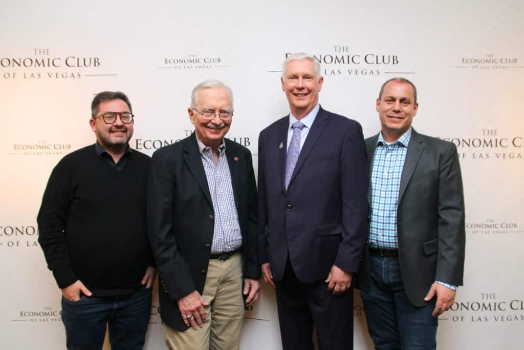 Four smiling men stand in front of a white wall with "THE ECONOMIC CLUB OF LAS VEGAS" repeated.