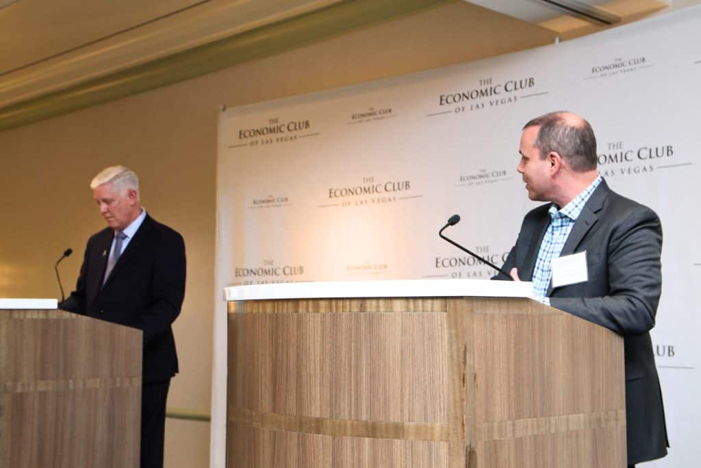 Two men stand at wooden podiums with microphones in front of a backdrop reading "The Economic Club of Las Vegas."
